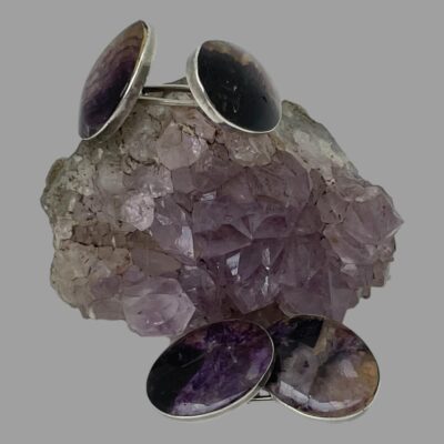 Close up of the cufflinks still displayed with a small rock of natural amethyst. One cufflink is on top of the amethyst rock and other is placed in the foreground in front of the rock.
