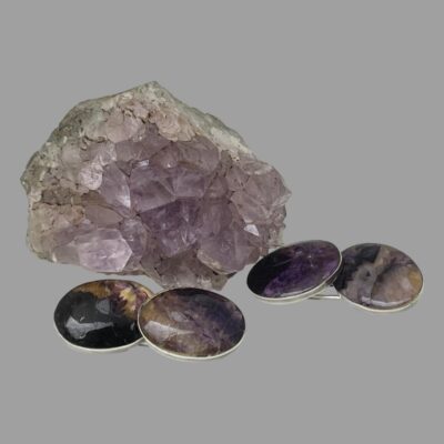Main photo of the 2 cufflinks laid in front of a small rock of natural amethyst with both ends of the Blue John on display. The Blue John has a range of purple colouring from dark purple to lilac even clear in places.