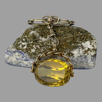 Main photo of fob shown with the pin and chain resting on top of a small natural rock and the large citrine stone in the foreground placed in front of the rock. The citrine has a lovely dark lemon colour. The gold appears to be both yellow and rose gold in 9 karat.