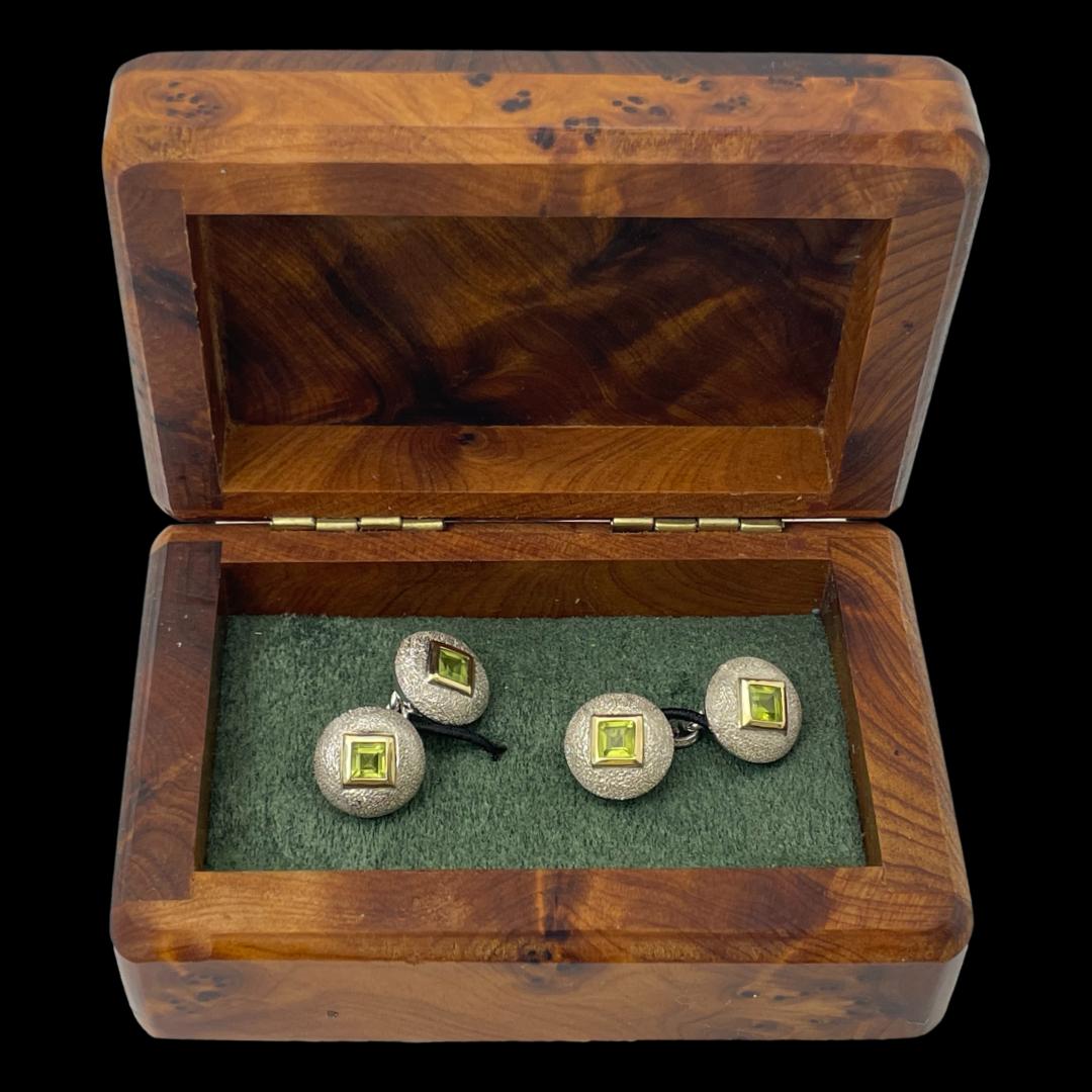 Main photo of cufflinks displayed inside the box. Looking straight down from above, the cufflinks are positioned to the left and right on green which is inside a walnut wood like box. The background is black.
