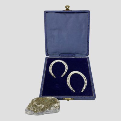 Main photo of the horseshoes displayed inside their fitted case and shown with the lid upright. The box is blue with a blue silk lining on inside lid and blue velvet where horseshoes sit. This would really make a perfect wedding present. (A small rock is to the left of the bottom of case which is holding the case at a slight upright angle.