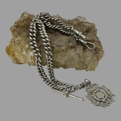 Main photo of chain displayed spread over a rock of natural quartz. The fob and t-bar are in the bottom right of the photo off the rock of quartz, The chain is laid across the rock and the dog clip ends are on the right on top of the rock. The graduating chains with the wider middle area is visible.